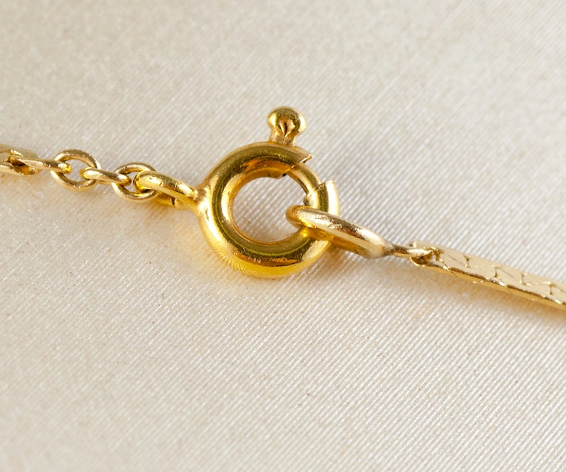 May include: Close-up of a gold chain necklace clasp. The clasp is a round, spring-loaded ring with a small, decorative piece on top.