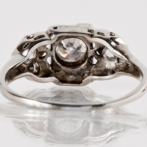 Puede incluir: Un anillo de plata con una gran piedra preciosa transparente rodeada de piedras preciosas m&aacute;s peque&ntilde;as. El anillo tiene un dise&ntilde;o delicado e intrincado.