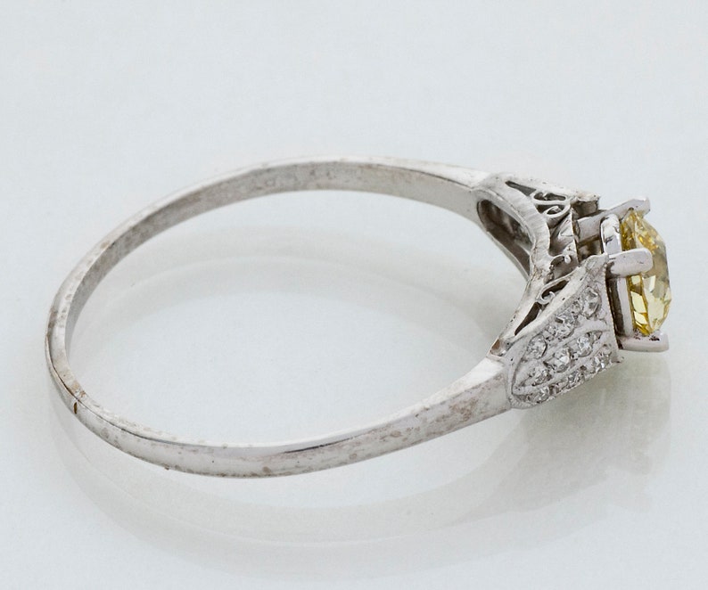 May include: A silver ring with a large, yellow gemstone and smaller clear stones. The ring has an ornate design on the sides of the gemstone and a simple band. The ring is set against a white background.