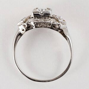 Puede incluir: Un anillo de plata con una piedra central grande de forma cuadrada y piedras m&aacute;s peque&ntilde;as a cada lado. El anillo est&aacute; engastado en un dise&ntilde;o delicado e intrincado.