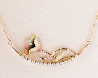 May include: Gold-tone necklace featuring a floral pendant with a pink, yellow, and green enamel flower, a small diamond, and a strand of pearls. The necklace has a delicate chain.