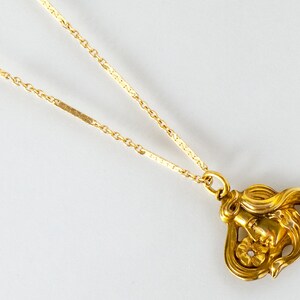 May include: A gold necklace with a pendant featuring a detailed, stylized image of a woman's face with a flower.