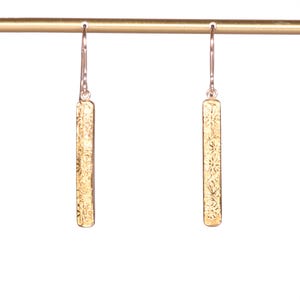 Könnte beinhalten: Goldene Bar-Ohrringe mit floralem Design. Die Ohrringe hängen an einer goldenen Stange.