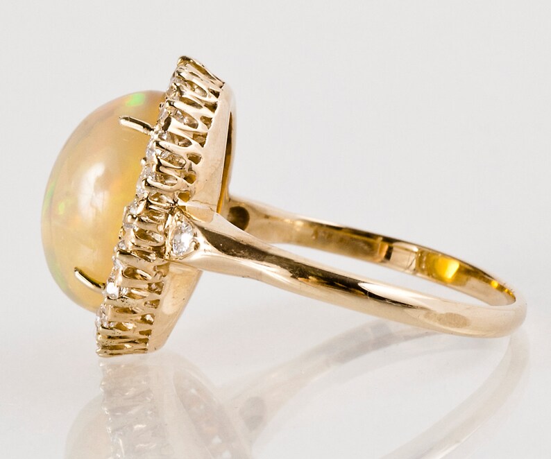 May include: A gold ring with a large oval opal gemstone surrounded by a halo of smaller diamonds.