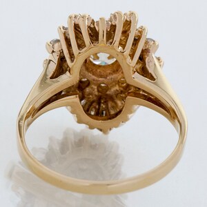 May include: A gold ring featuring a central, oval-shaped gemstone surrounded by smaller stones. The ring's band is a smooth, polished gold, and the setting has a detailed, textured design. The ring is likely a piece of jewelry.