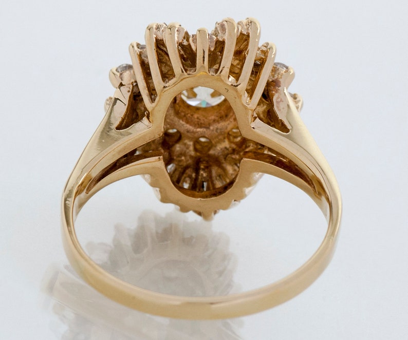 May include: A gold ring featuring a central, oval-shaped gemstone surrounded by smaller stones. The ring's band is a smooth, polished gold, and the setting has a detailed, textured design. The ring is likely a piece of jewelry.