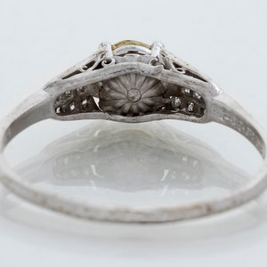 May include: A vintage silver ring with a central yellow gemstone and smaller accent stones. The ring features intricate filigree detailing around the main stone and along the band, showcasing a classic, elegant design. The ring is set against a white background.