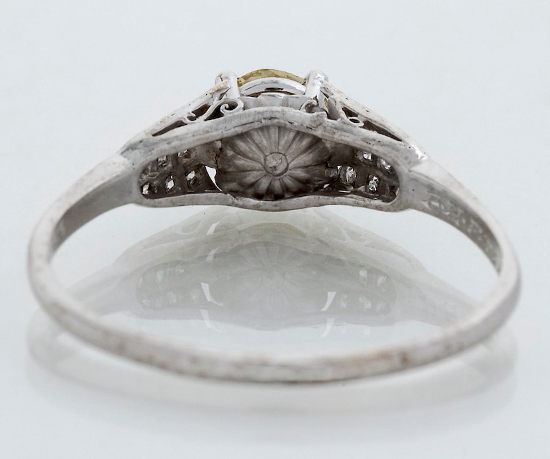 May include: A vintage silver ring with a central yellow gemstone and smaller accent stones. The ring features intricate filigree detailing around the main stone and along the band, showcasing a classic, elegant design. The ring is set against a white background.