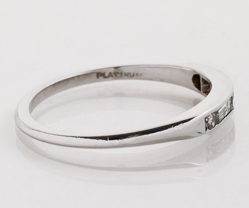 May include: A platinum band ring with a row of small, rectangular diamonds set in the band. The ring is marked "PLATINUM" on the inside.