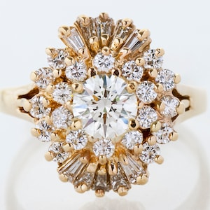 May include: A gold ring featuring a large, round, brilliant-cut diamond at the center, surrounded by smaller diamonds and baguette-cut diamonds. The ring has a sunburst or floral design, with a polished gold band.