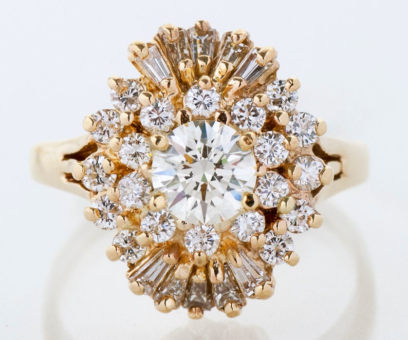May include: A gold ring featuring a large, round, brilliant-cut diamond at the center, surrounded by smaller diamonds and baguette-cut diamonds. The ring has a sunburst or floral design, with a polished gold band.