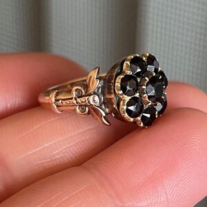 May include: A gold ring featuring a cluster of black gemstones set in a flower design.