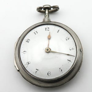 Könnte beinhalten: Eine silberne Taschenuhr mit weißem Zifferblatt und schwarzen römischen Ziffern für die Stunden. Die Uhr hat einen goldfarbenen Sekundenzeiger und einen silberfarbenen Minutenzeiger.