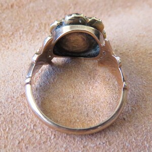 May include: A gold ring with a round, raised centre and a decorative band. The ring is set with small, round stones.
