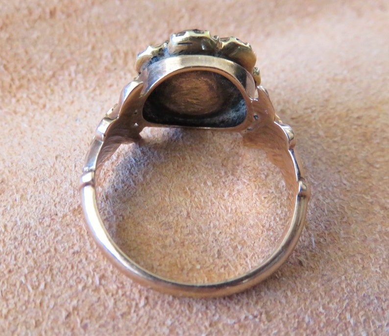 May include: A gold ring with a round, raised centre and a decorative band. The ring is set with small, round stones.