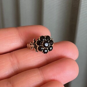 May include: A gold ring with a flower-shaped design set with black gemstones.