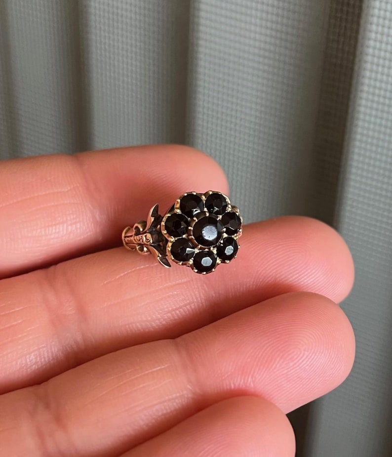 May include: A gold ring with a flower-shaped design set with black gemstones.
