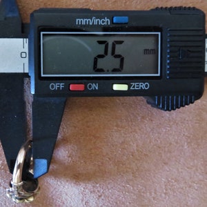 May include: A close-up of a digital caliper measuring a ring. The caliper reads 2.5 mm.