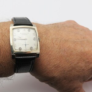 May include: A vintage rectangular wristwatch with a silver-toned case and a black leather band. The watch face is off-white with silver hands and hour markers. The brand name "MICHAEL'S" is printed on the watch face.