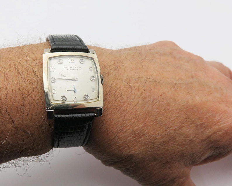 May include: A vintage rectangular wristwatch with a silver-toned case and a black leather band. The watch face is off-white with silver hands and hour markers. The brand name "MICHAEL'S" is printed on the watch face.