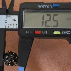 May include: A black and gold button with a diameter of 12.5 millimetres, measured with a digital caliper.