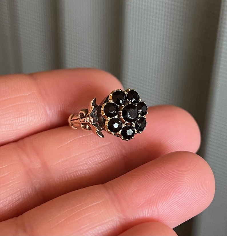 May include: A gold ring featuring a black flower-shaped cluster of gemstones. The ring has an intricate design on the band.