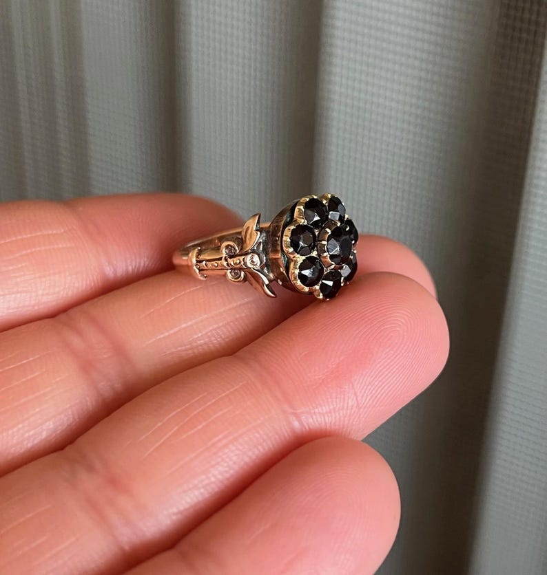 May include: A gold ring featuring a cluster of black gemstones set in a flower design.