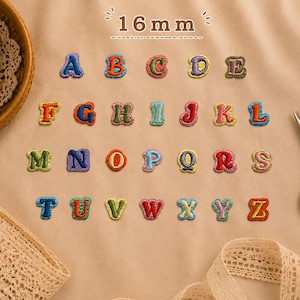 May include: A set of twenty-six embroidered alphabet letter patches, each measuring 16mm in height. The letters are arranged in rows, featuring various vibrant colors and stitched borders. A spool of thread and metal scissors are also present.