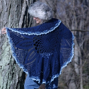May include: A navy blue crocheted shawl with a scalloped light blue trim. The openwork design features a circular pattern in the center. The shawl is draped over the shoulders.