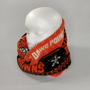 May include: Orange and black fleece infinity scarf with the words "DAWG POUND" printed on it. The scarf has a repeating pattern of snowflakes and a geometric design.