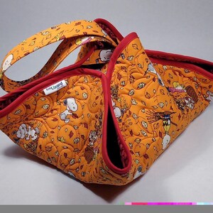 May include: Orange quilted tote bag with a red trim and handles. The bag features a repeating pattern of Snoopy and fall leaves. The interior is red, and the bag has a label that says "little lizard".