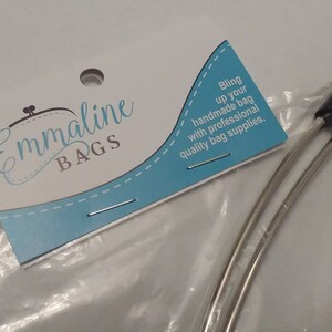 May include: Bag-making supplies, including two silver-toned metal handles with black tips, are packaged with a white and light blue Emmaline Bags tag. The tag includes the text: "Bling up your handmade bag with professional quality bag supplies."