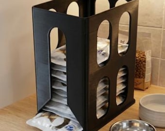 Peut inclure: Un organisateur de rangement vertical noir avec des découpes rectangulaires arrondies sur les côtés, contenant une pile de sachets alimentaires rectangulaires blancs. L'organisateur présente une ouverture frontale pour distribuer les sachets.