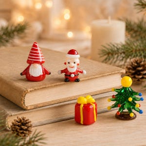 May include: A collection of miniature glass figurines including a red and white striped gnome, a Santa Claus figure, a red gift box with a yellow ribbon, and a green Christmas tree with multicolored glass ornaments arranged on two stacked books.
