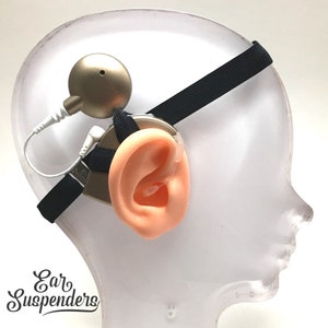 Puede incluir: Una correa negra con un auricular beige y un cable blanco conectado a un micrófono beige. La correa se lleva sobre la cabeza y el auricular se coloca sobre la oreja. El micrófono está posicionado cerca de la boca. El texto "Ear Suspenders" es visible en la esquina inferior izquierda de la imagen.