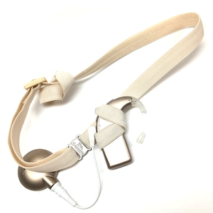 May include: A beige hearing aid strap with a beige hearing aid attached. The hearing aid has a white cord attached to a beige device with the text "Baby Whisperer" on it.