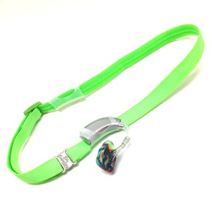 Puede incluir: Una correa de cuello verde con un audífono plateado y un molde de oído colorido adjunto. La correa tiene el texto "Life Sounds" impreso en la hebilla.