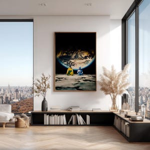 May include: A framed wall art print featuring two figures in yellow and blue clothing sitting on a lunar surface, looking up at a large, glowing Earth against a black space background. The artwork is displayed in a modern, bright living room.