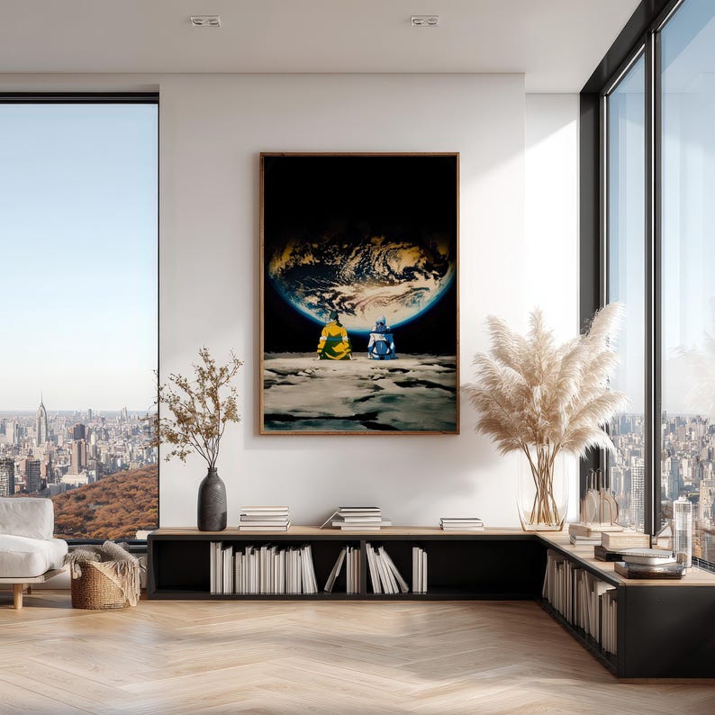 May include: A framed wall art print featuring two figures in yellow and blue clothing sitting on a lunar surface, looking up at a large, glowing Earth against a black space background. The artwork is displayed in a modern, bright living room.
