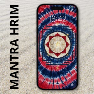May include: A smartphone displaying a tie-dye wallpaper with red and blue swirls. Centered is a circular yantra design featuring a red lotus, geometric patterns, and the golden Sanskrit syllable Hrim. The text MANTRA HRIM is visible on the left.