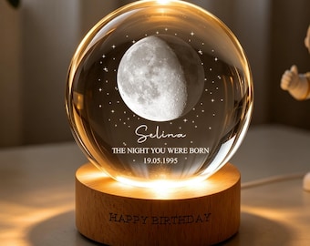 May include: A clear glass sphere featuring an etched moon and stars, personalized with the name Selina, the text THE NIGHT YOU WERE BORN, and the date 19.05.1995. The sphere sits on a round wooden base engraved with the text HAPPY BIRTHDAY.