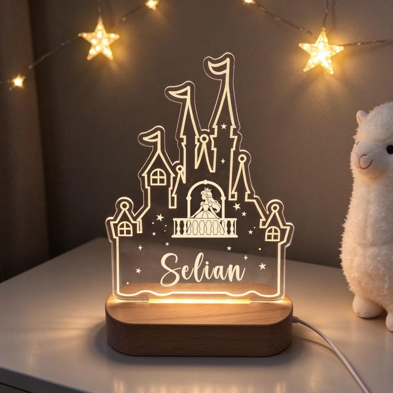 Puede incluir: Una luz nocturna de acr&iacute;lico transparente con forma de castillo, una silueta de princesa en un balc&oacute;n y el nombre Selian grabado en blanco. La luz est&aacute; montada sobre una base de madera ovalada y lisa con un cable de alimentaci&oacute;n lateral.
