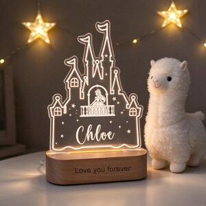 Puede incluir: Una luz nocturna de acr&iacute;lico transparente con forma de castillo, una silueta de princesa, el nombre Chloe y estrellas grabadas. Se apoya en una base de madera con el texto grabado Love you forever, junto a una llama de peluche blanca.
