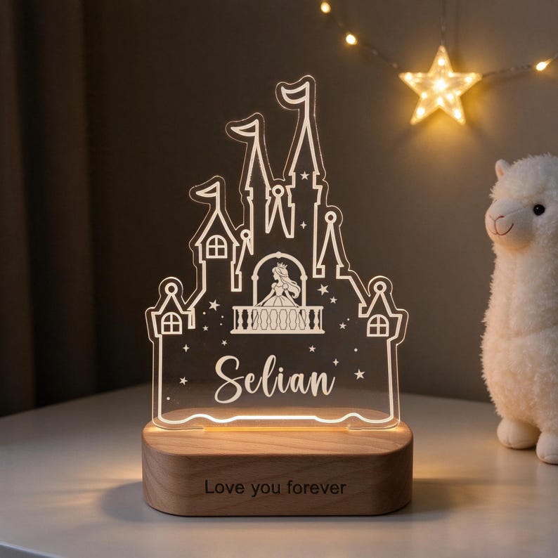 Puede incluir: Una luz nocturna de acr&iacute;lico transparente con la silueta de un castillo grabada, una figura de princesa en un balc&oacute;n y el nombre Selian. La luz se asienta sobre una base de madera clara grabada con el texto Love you forever.