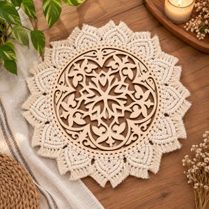 May include: A circular wall hanging featuring a light-coloured wooden centre with an intricate laser-cut floral pattern, surrounded by a thick, cream-coloured macrame border with knotted fringe details arranged in a repeating scalloped design.