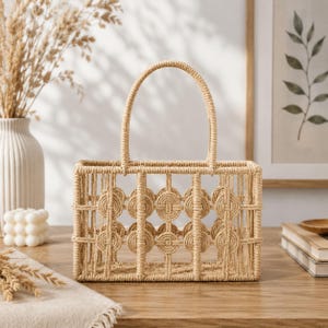 May include: A rectangular basket crafted from light tan woven rope, featuring a structured open-grid design with circular accents and a single arched handle. The basket has a rigid frame and a consistent natural fibre texture throughout its construction.