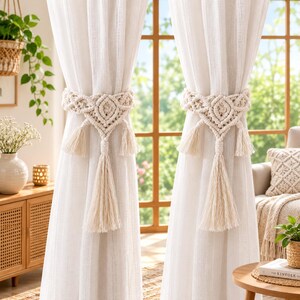 May include: A pair of off-white macrame curtain tiebacks featuring intricate knotted patterns, diamond-shaped centers, and long hanging tassels. These decorative textile accessories are designed to hold back light-colored fabric curtains.