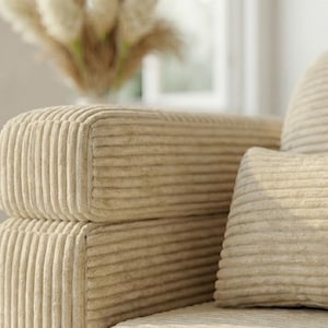 May include: A beige corduroy sofa featuring a distinct vertical ribbed texture on the armrest and a matching rectangular throw pillow. The fabric has a soft, plush appearance with consistent parallel lines running across the entire surface.