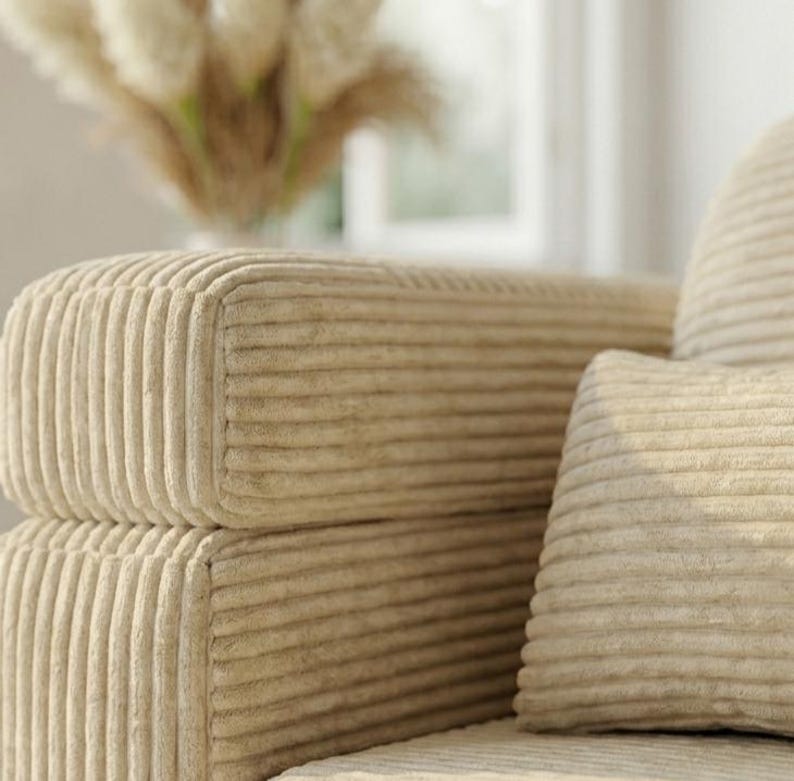 May include: A beige corduroy sofa featuring a distinct vertical ribbed texture on the armrest and a matching rectangular throw pillow. The fabric has a soft, plush appearance with consistent parallel lines running across the entire surface.