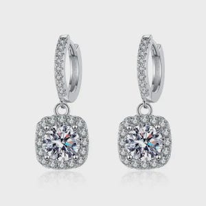 May include: A pair of silver-toned hoop earrings featuring a hinged closure and a square-shaped drop pendant. Each earring is encrusted with small clear stones along the hoop and a larger round clear stone centered in the square pendant frame.